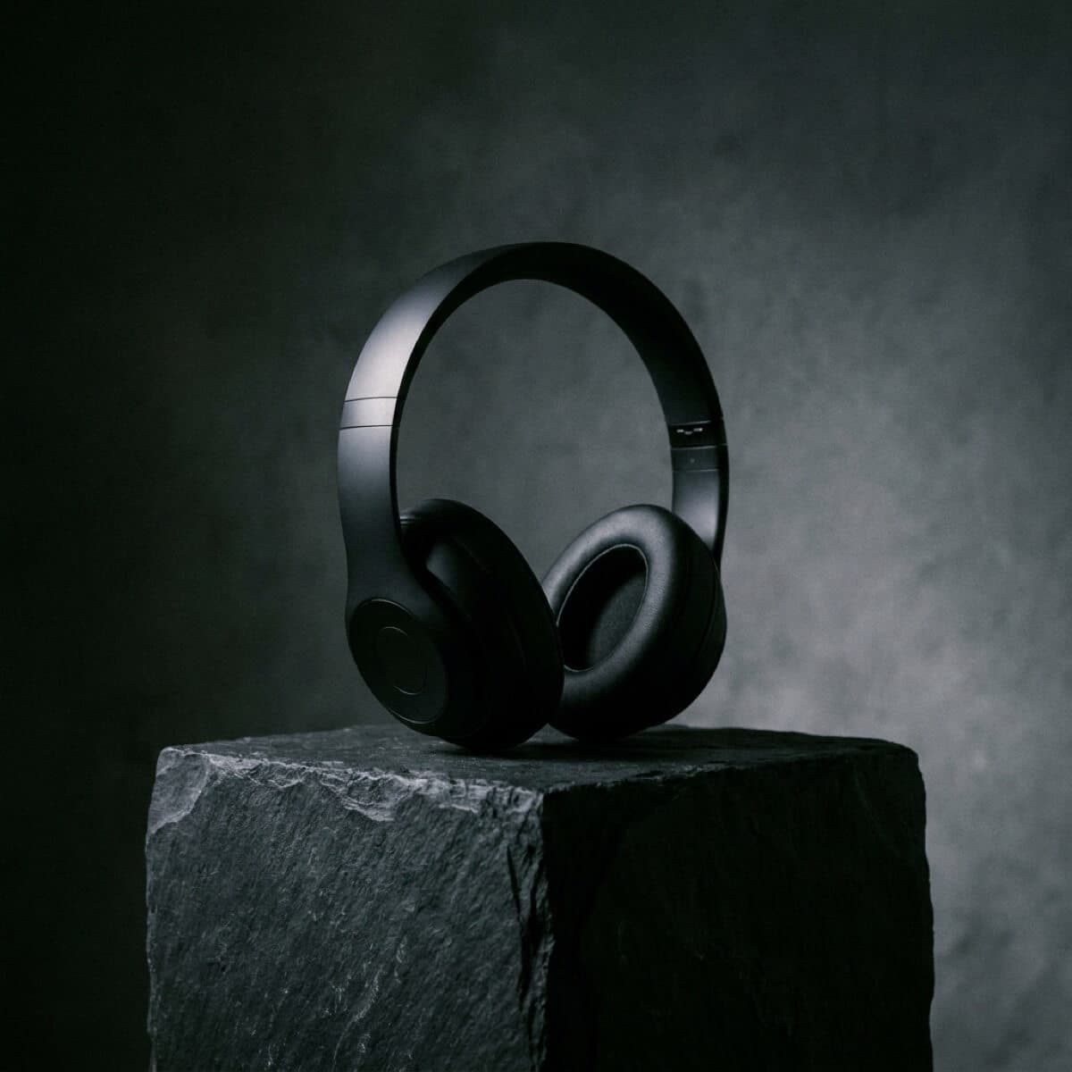 Product photo of matte black wireless headphones on a stone pedestal, dramatic side lighting — Lighting control